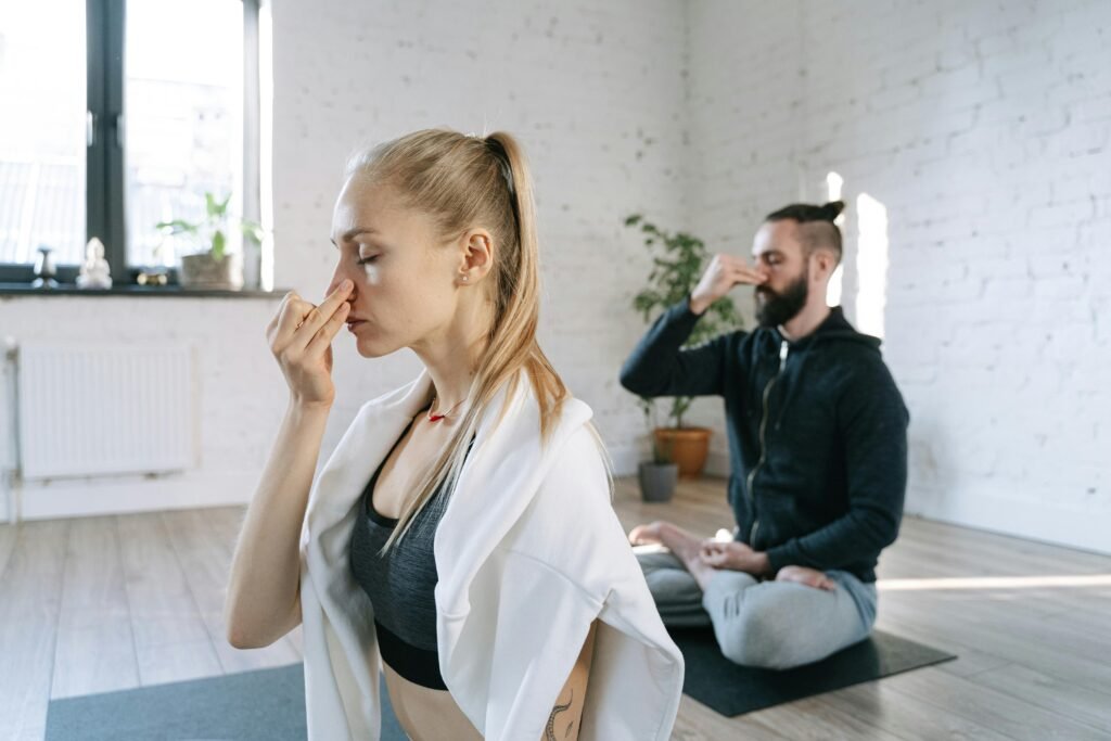 Two individuals practicing mindful breathing yoga in a serene indoor home setting.