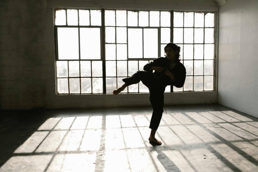 A martial artist in action, practicing kicks in a sunlit studio with shadow patterns.
